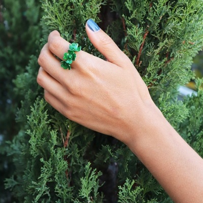 Anel verde com flores num dedo em fundo de folhagem