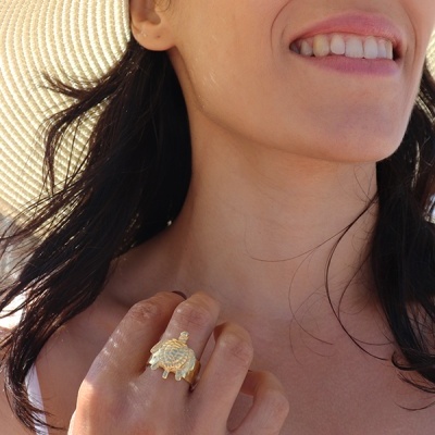 Anel dourado com design de tartaruga na mão de mulher com chapéu de palha