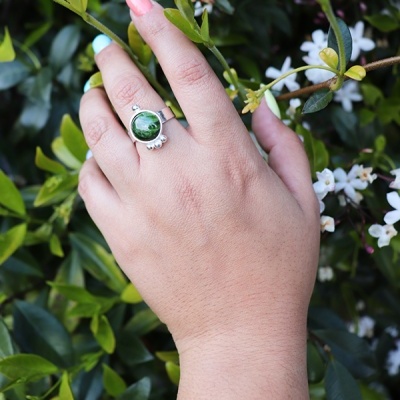 Anel prateado com pedra verde em mão com unhas coloridas segurando ramo com flores