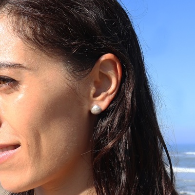 Brinco prateado em formato de concha usado em orelha de mulher junto ao mar