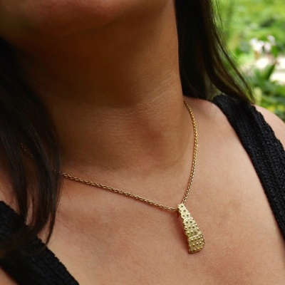 Colar dourado com pendente texturizado usado por mulher com top preto