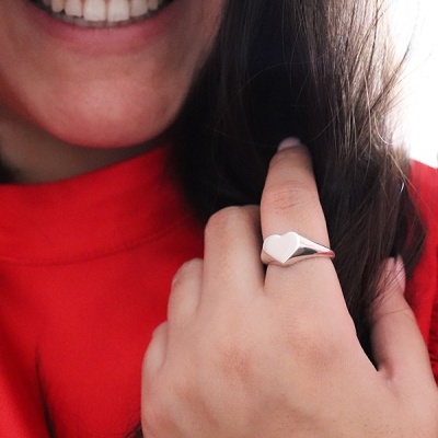 Anel prateado com coração no dedo médio e pessoa sorrindo com camisola vermelha