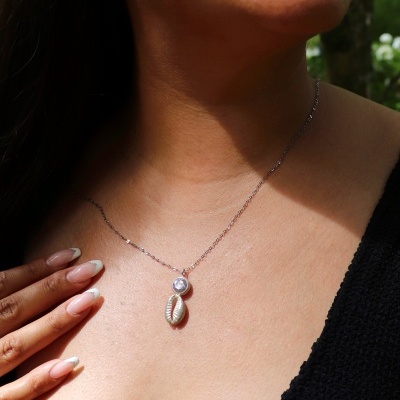 Colar prateado com pendente de pedra clara e concha em pescoço feminino