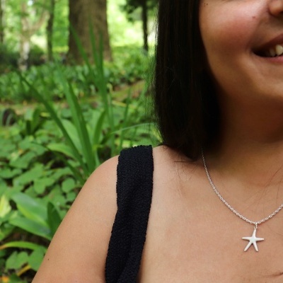 Colar prateado com pendente estrela-do-mar em mulher com vestido preto em ambiente natural