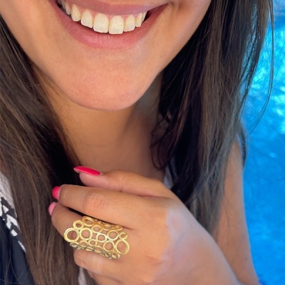 Anel dourado com padrão de círculos na mão de mulher com unhas vermelhas