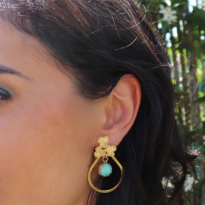 Brinco dourado com flores e pedra turquesa na orelha esquerda