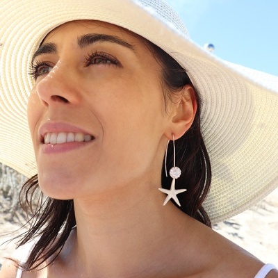 Brincos dourados pendentes com estrela-do-mar e pedra brilhante usados por mulher com chapéu branco