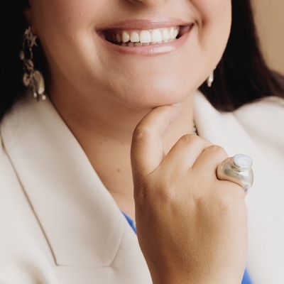Mulher sorridente com anel prateado de pedra branca na mão.