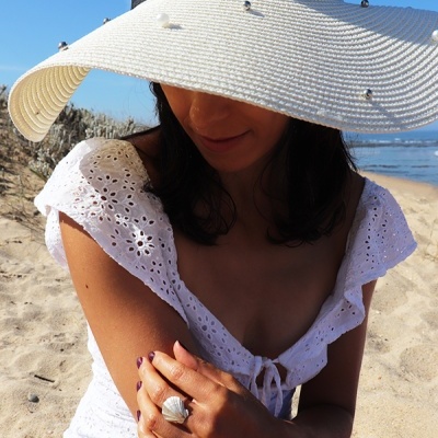 Mulher na praia com chapéu branco e vestido branco rendado