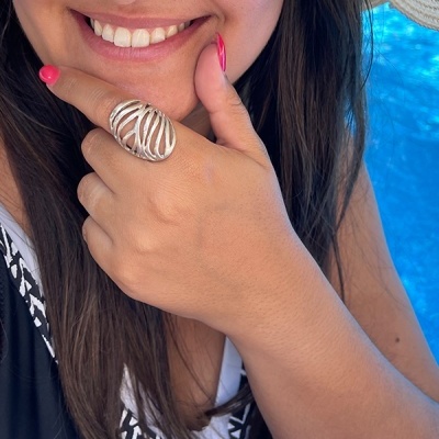 Mulher a usar anel prata com design aberto e esmalte rosa, perto de piscina azul