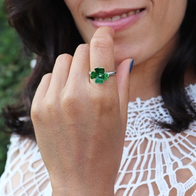 Anel prateado com flor verde em dedo de mulher com roupa branca em renda