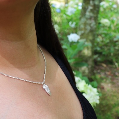Colar prateado com pendente em forma de concha, top preto, fundo de vegetação