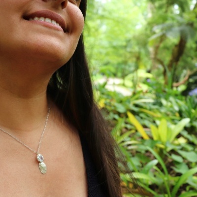 Colar prateado com pendente de folha e pedra transparente em pescoço feminino com fundo verde natural
