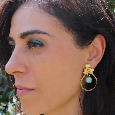 Brincos dourados com flores e pedra azul em orelha feminina