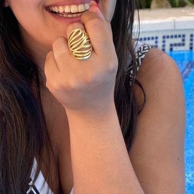 Mulher com anel dourado ondulado à mão à frente do rosto junto a piscina
