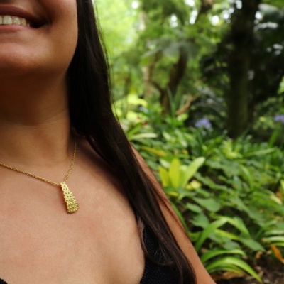 Colar dourado com pendente texturizado usado no pescoço de mulher