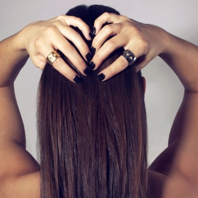 Anéis dourado e prateado com recortes de corações em mãos femininas com unhas pretas e cabelo castanho.