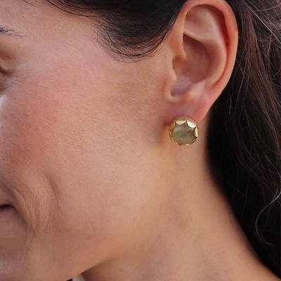 Brinco dourado redondo com superfície facetada na orelha de mulher