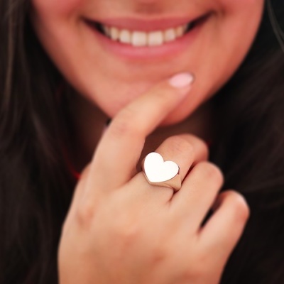 Anel de coração prateado liso no dedo de uma mulher sorridente
