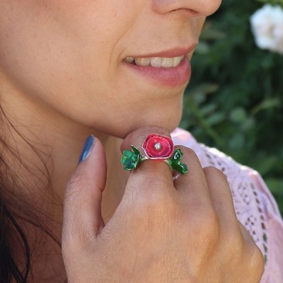 Anel artesanal com flor vermelha e folhas verdes em dedo de mulher