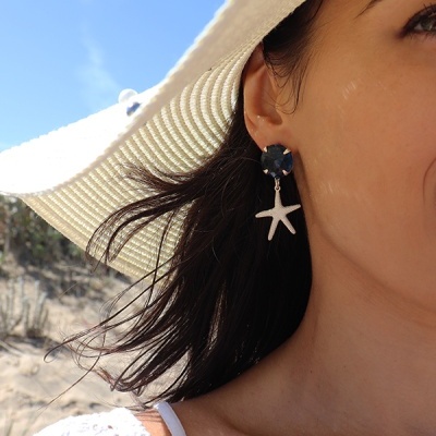 Brincos com estrela-do-mar e pedra azul usados por mulher na praia com chapéu branco