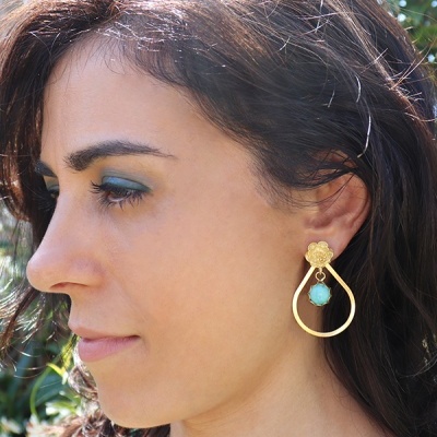 Brincos dourados com pendente azul turquesa usados por mulher