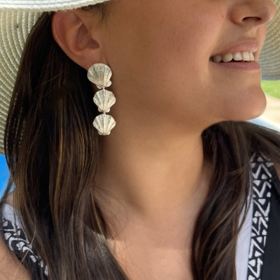 Mulher com chapéu branco e brincos prateados em forma de conchas