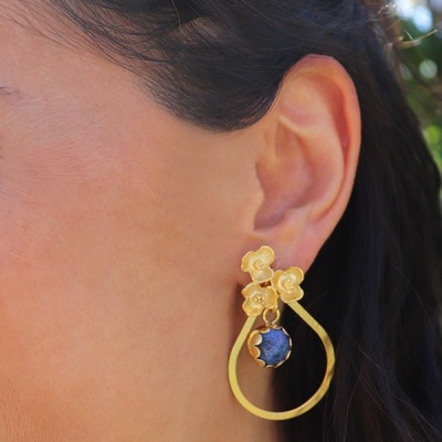 Brinco dourado com flores e pedra azul escura na orelha de mulher