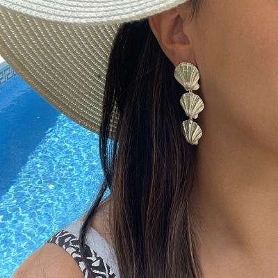Brincos com conchas douradas e chapéu branco com pérolas junto a piscina