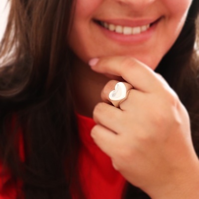 Anel de prata em forma de coração na mão de uma mulher sorridente com camisola vermelha