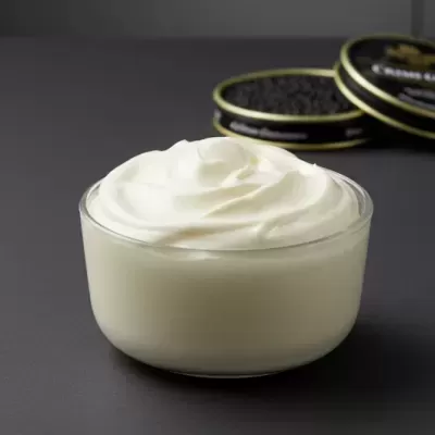 Taça com creme branco em frente a latas abertas de caviar negro sobre superfície cinza