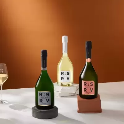 Garrafas de champanhe Maison Mumm RS RV com taças, bowl e vela em fundo castanho
