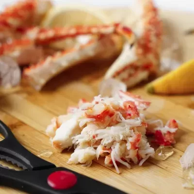 Carne de caranguejo desfiada sobre tábua de madeira com tesoura preta e limão amarelo.