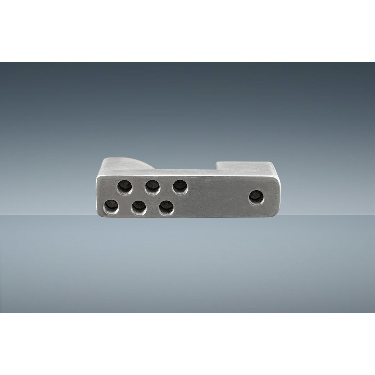 Peça metálica cinzenta com vários orifícios sobre superfície espelhada