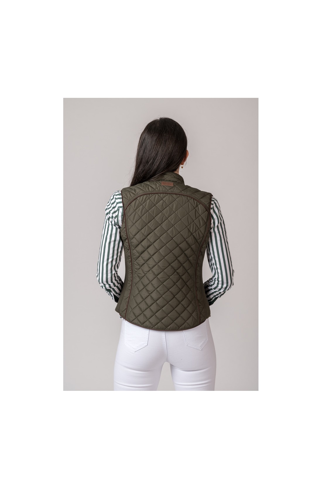 Colete acolchoado verde-oliva visto de costas com mulher usando camisa às riscas e calças brancas