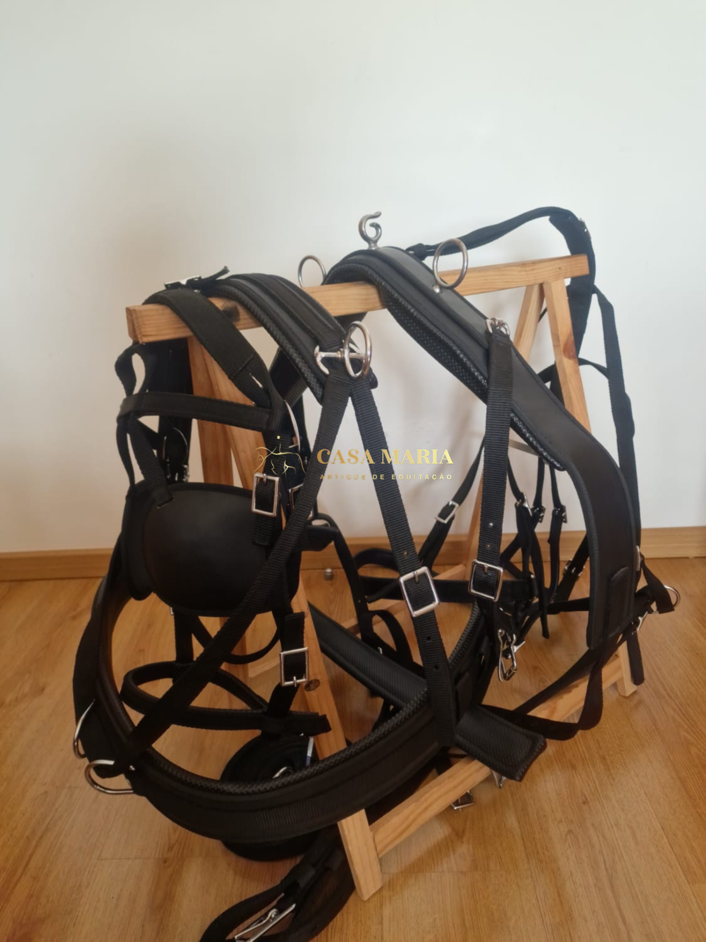 Arnês de couro preto e nylon com fivelas metálicas sobre suporte de madeira