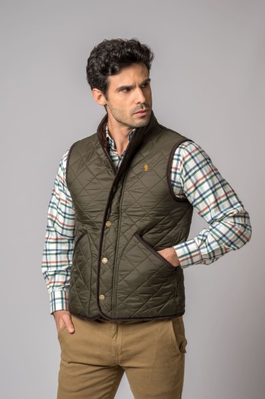 Colete masculino verde-oliva acolchoado com botões dourados sobre camisa xadrez e calças castanho claro