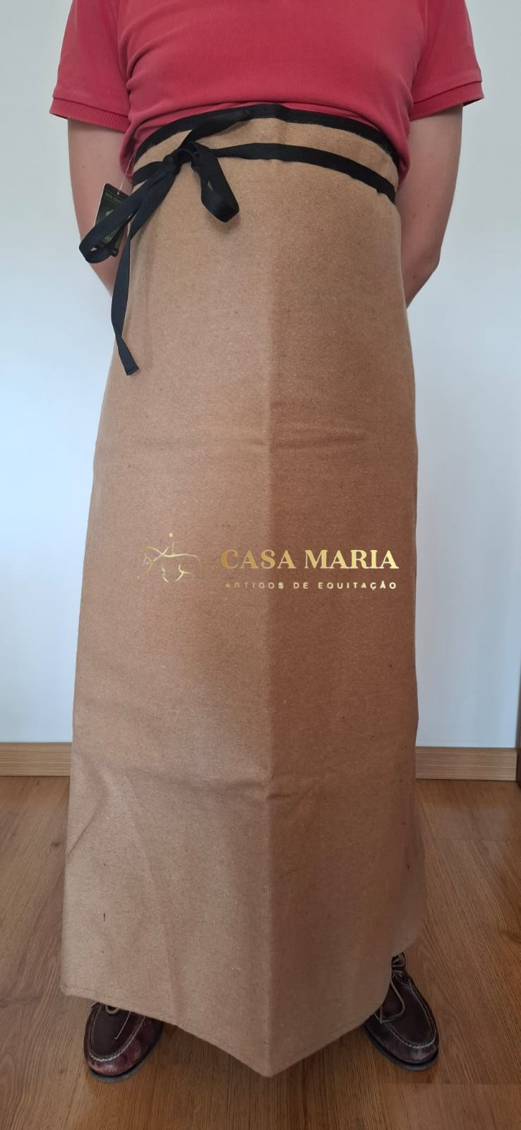 Saia longa castanha clara com cordões pretos e texto CASAMARIA AMIGOS DE EQUITAÇÃO, usada por pessoa com camisa vermelha