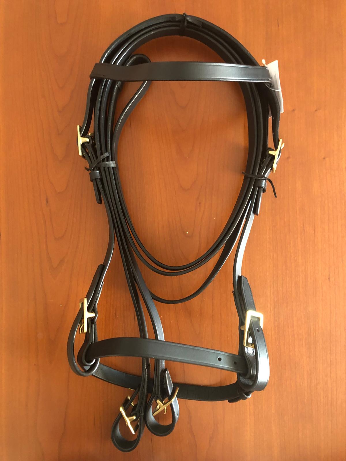Bridão em couro preto com fivelas douradas sobre mesa de madeira