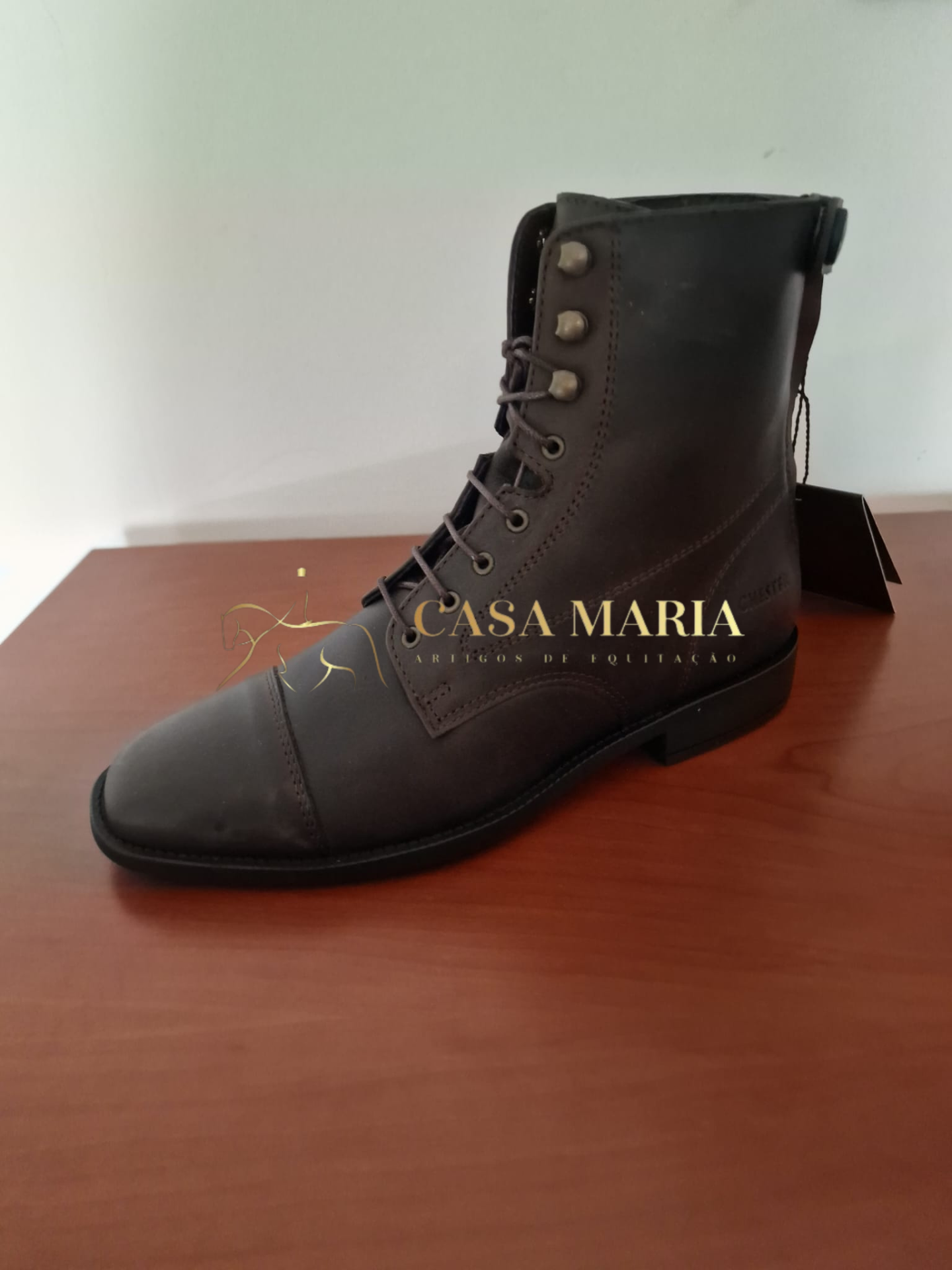 Bota de couro castanho escuro com atacadores sobre superfície de madeira.