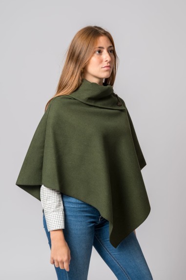 Poncho verde-oliva feminino com gola alta e botão, sobre camisa branca quadriculada e jeans azuis