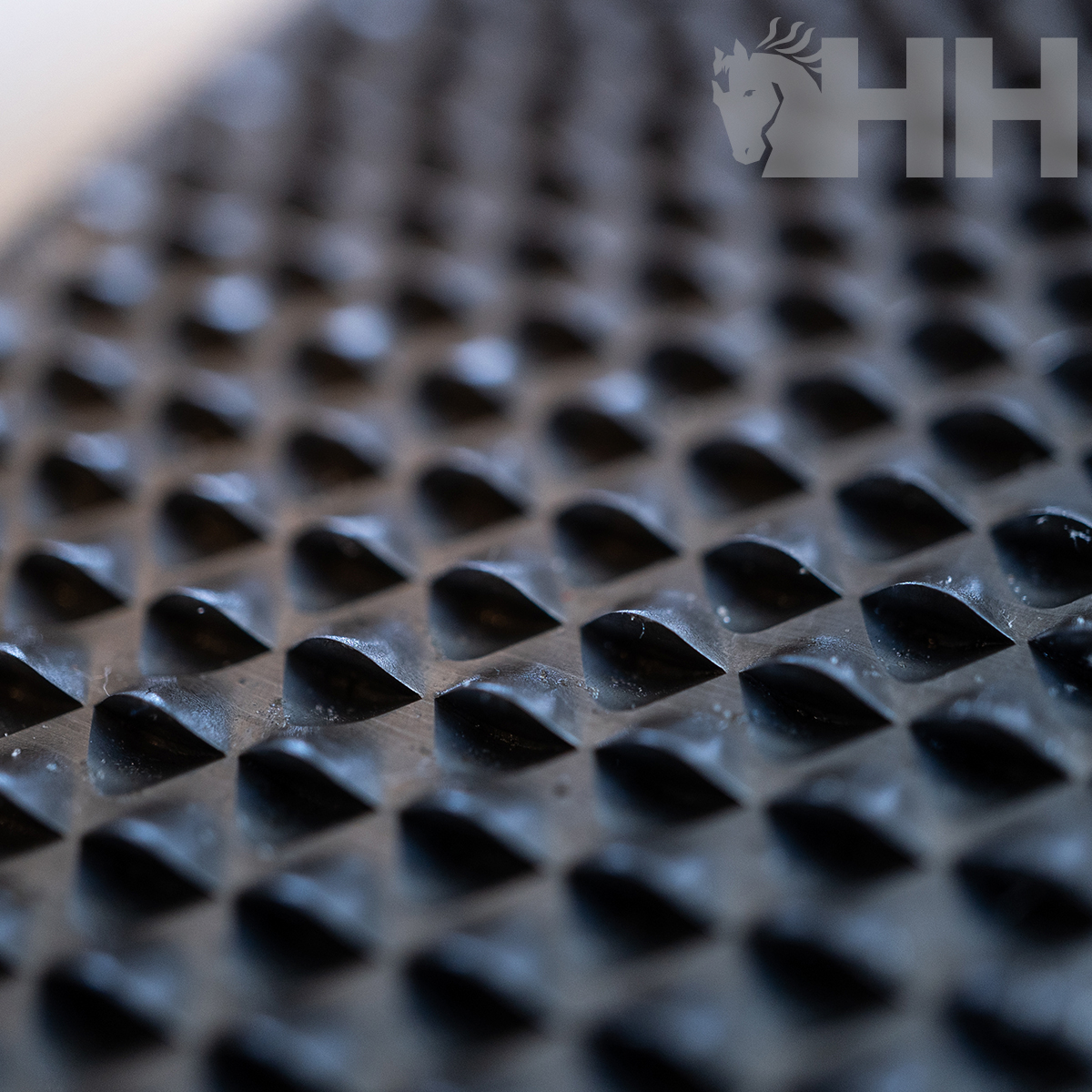 Superfície antiderrapante preta com padrão de quadrados escavados e logotipo HH