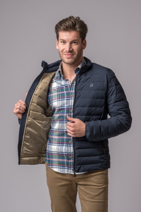 Homem com casaco acolchoado azul escuro aberto mostrando interior bege, camisa xadrez e calças castanho claro