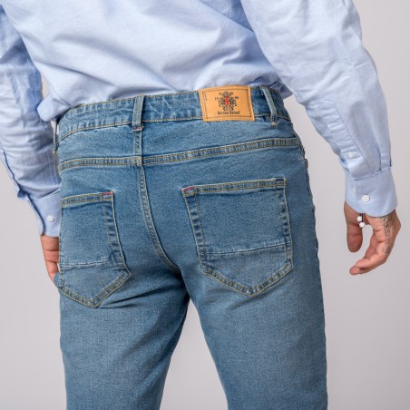 Jeans azuis em ganga com bolso traseiro e etiqueta de couro castanho, pessoa de camisa azul clara