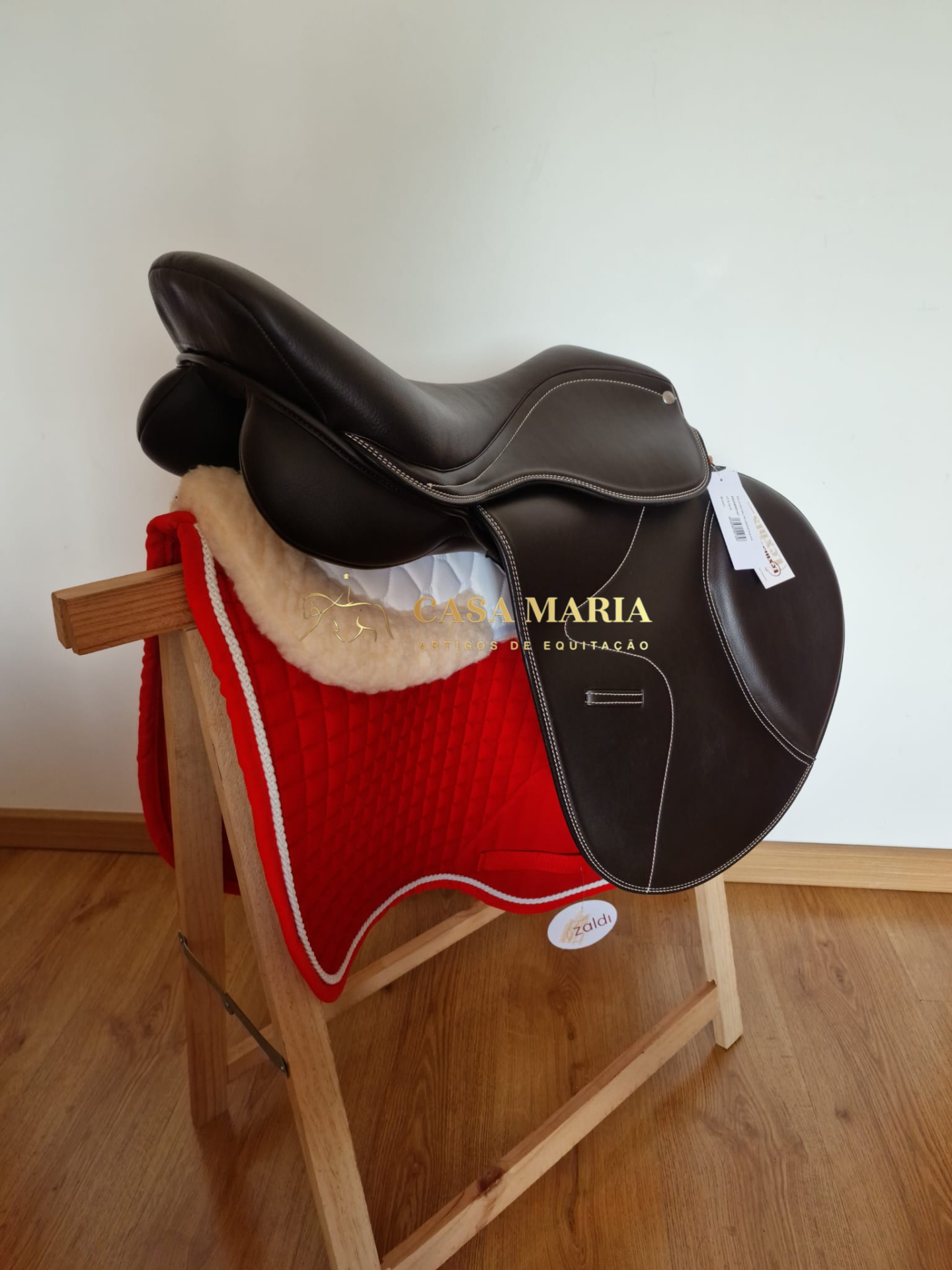 Sela de equitação castanha escura sobre manta vermelha em suporte de madeira