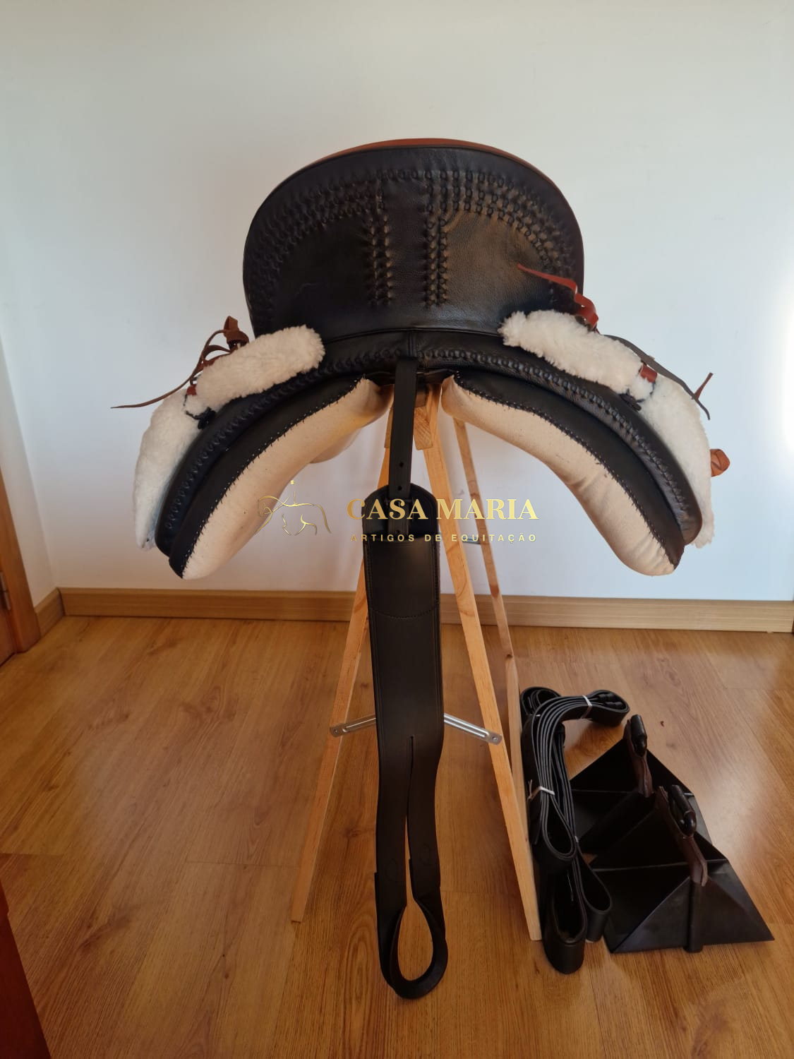 Sela de montaria preta em couro com forro branco sobre suporte de madeira