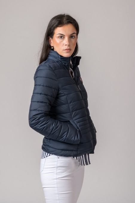 Casaco acolchoado azul escuro, mulher com calças brancas, fundo cinzento