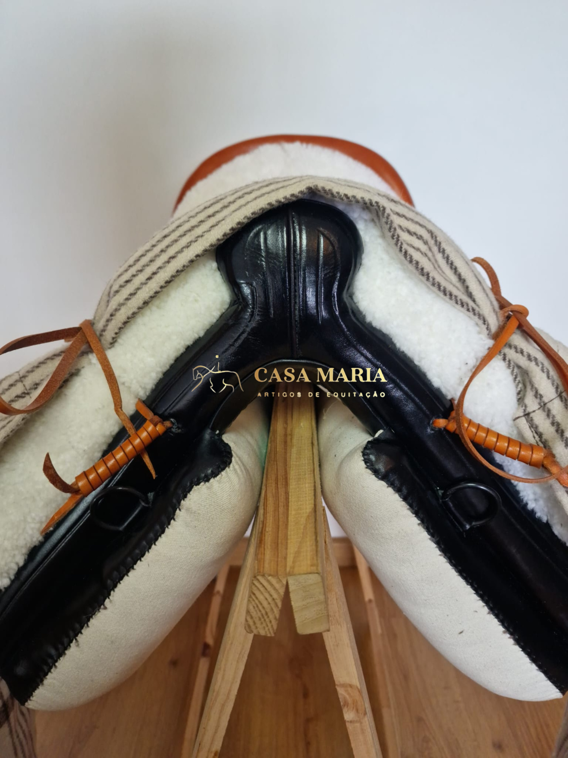 Sela de equitação castanha e preta com almofadas brancas sobre suporte de madeira