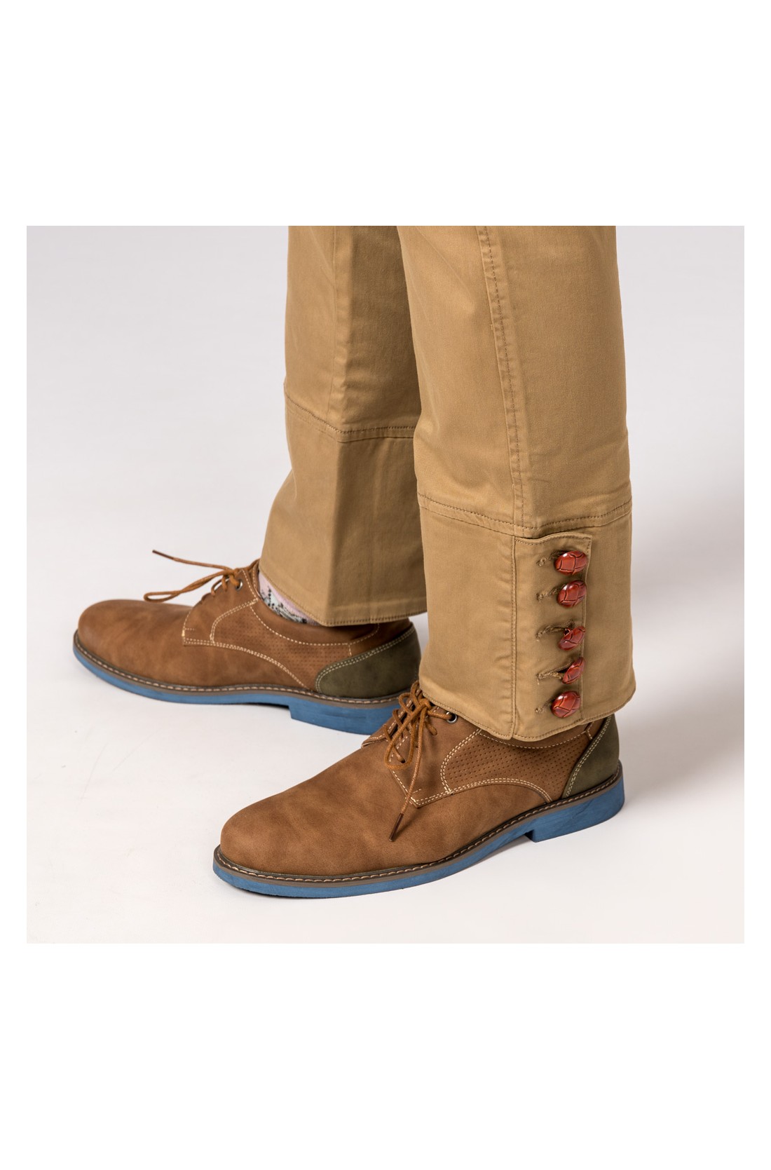 Pantalonas castanhas claras com botões vermelhos e sapatos castanhos com sola azul.