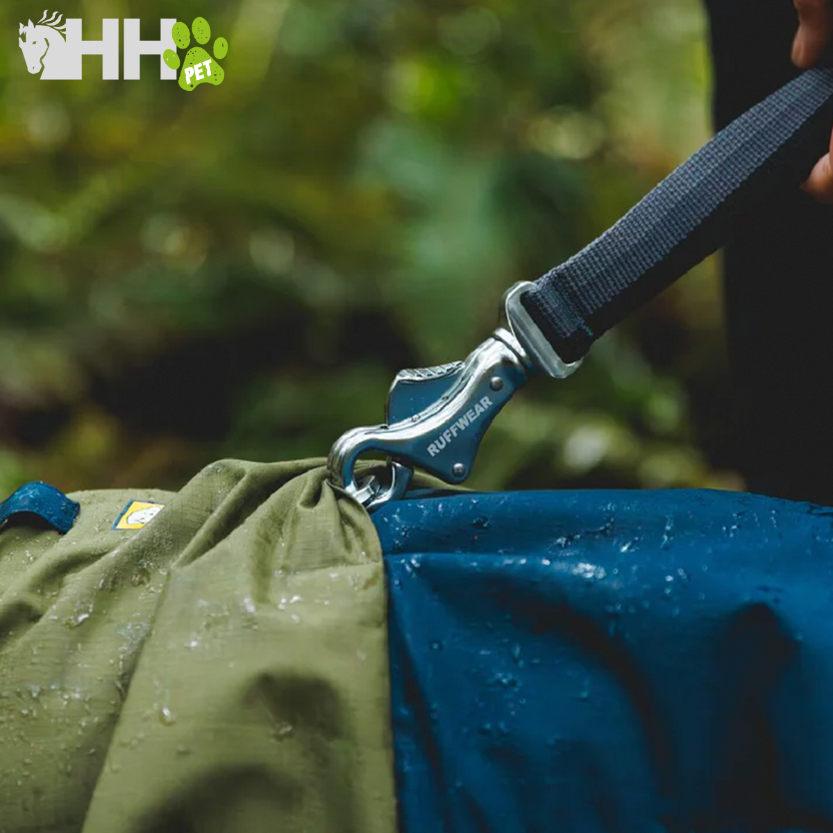 Gola/collier azul com fecho metálico RUFFWEAR preso a tecido verde ao ar livre com gotas de água